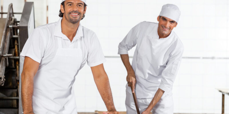 Portrait of happy male Baker's in uniform cleaning bakery